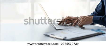 young business man Recording data on laptop, comparing details from graphs. Business income charts in the areas of real estate, tax, management, technology marketing in a private office.