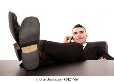 Young business man relaxing at office desk and talking on mobile phone, isolated on white