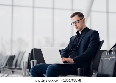 Young Business Man Sitting On The Computer With Modern Stylish Wireless Earphones At The Airport Waiting For The Flight