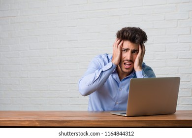 Young business man sitting and working on a laptop frustrated and desperate, angry and sad with hands on head