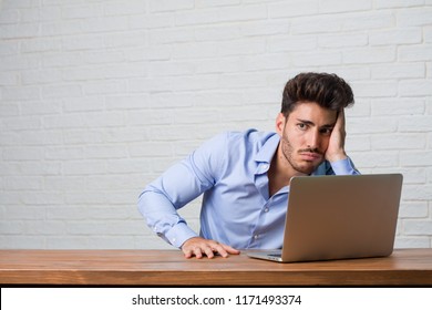 Young business man sitting and working on a laptop frustrated and desperate, angry and sad with hands on head