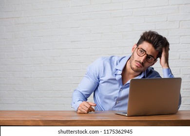 Young business man sitting and working on a laptop worried and overwhelmed, forgetful, realize something, expression of shock at having made a mistake