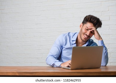 Young business man sitting and working on a laptop laughing and having fun, being relaxed and cheerful, feels confident and successful