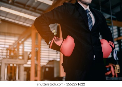 A young business man in a suit, shirt and tie at an industrial factory He wears boxing gloves, demonstrating unceasing preparation for the fight for business progress. - Shutterstock ID 1552291622
