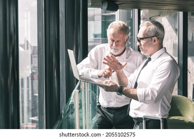 Young Business Man Taking To His Older Business Man Partner. They Are In White Shirt And Black Tie. They Are In A Hotel Lobby. 