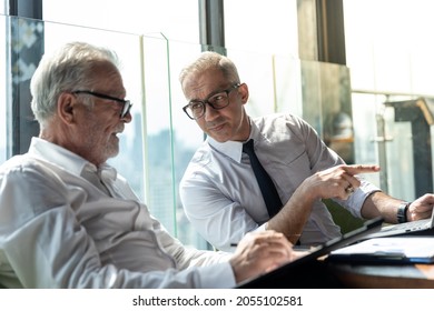 Young Business Man Taking To His Older Business Man Partner. They Are In White Shirt And Black Tie. They Are In A Hotel Lobby. 