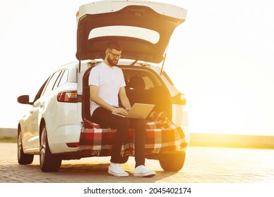 Young business man using a laptop laptop to work in the trunk of a car, enjoying the trip, travel and weekend adventures