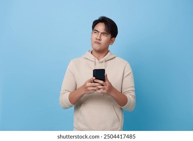 Young business man using mobile cell phone ponders on how to answer question, thinks deeply about something looking isolated on blue background. - Powered by Shutterstock