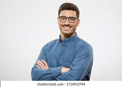 Young Business Man Wearing Blue Shirt And Glasses, Looking At Camera With Positive Confident Smile, Holding Arms Crossed, Isolated On Gray Background