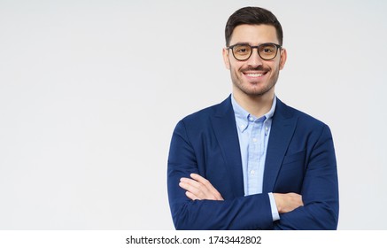 Young Business Man Wearing Formal Clothes And Glasses, Looking Straight At Camera With Smile, Holding Arms Crossed, Isolated On Gray Background, Copyspace On Left