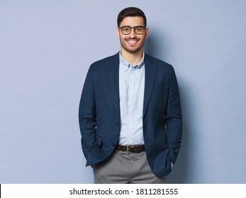 Young business man wearing formal clothes and eyeglasses, standing isolated against blue background in relaxed pose, smiling friendly - Shutterstock ID 1811281555