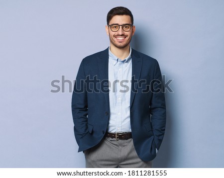 Young business man wearing formal clothes and eyeglasses, standing isolated against blue background in relaxed pose, smiling friendly