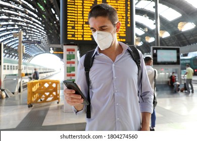 Young business man wearing KN95 FFP2 face mask at train station. Young caucasian man with behind timetables of departures arrivals using smart phone in train station. - Powered by Shutterstock