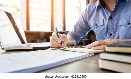 Young Business Man Working In Bright Office, Using Laptop, Writing Notes.