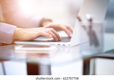 Young business man working on a laptop at his desk in the office, in view of the profile against the window