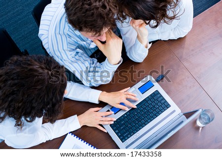 Young business people sitting by table at office, working together on laptop computer. High-angle view.