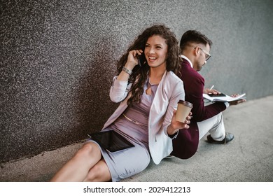 Young Business People Sitting Down In Front Of A Modern Office Building 