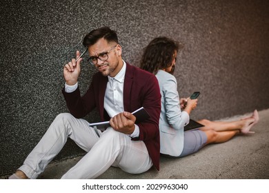 Young Business People Sitting Down In Front Of A Modern Office Building 