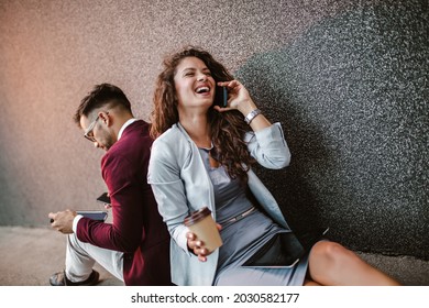 Young Business People Sitting Down In Front Of A Modern Office Building 