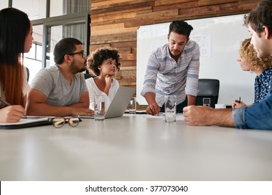 Young Business Team In A Meeting Discussing Progress Of The Company. Creative Professionals Sitting Around A Table In Office.