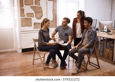 Young business team sitting in a semi circle sharing fresh ideas while everyone is looking at the lady explaining something to them