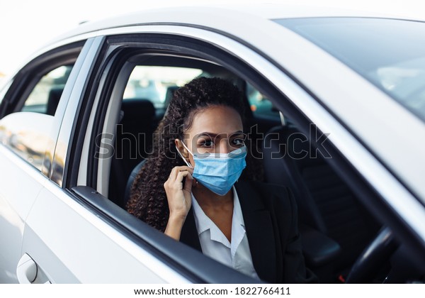 Young business woman\
behind the steering wheel of a taxi adjusts the medical mask.\
Business trips during pandemic, new normal and coronavirus travel\
safety concept.