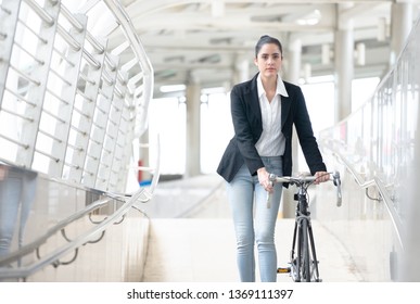 Young business woman with bike walking along sidewalk outdoors in urban city, Pushing Bike City Concept.