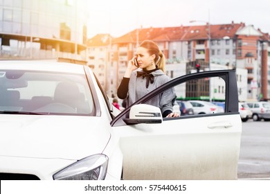 Young Business Woman Casually Dressed Getting In Her Car. Beautiful Young Woman Making A Phone Call From The Parking Lot. Lens Flare In The Background.