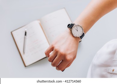 A young business woman checks time on her classic watch, she thinks about time management and corrects schedule in her diary - Shutterstock ID 412714360