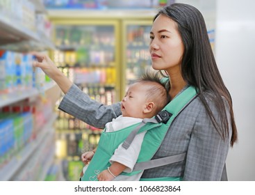 Young Business Woman Choosing Breakfast In Convenience Store While Carrying Her Baby Boy By Hipseat.