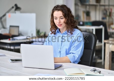 Young business woman company employee sitting at desk working on laptop. Busy female professional worker marketer using computer in corporate modern office managing data technology operations.