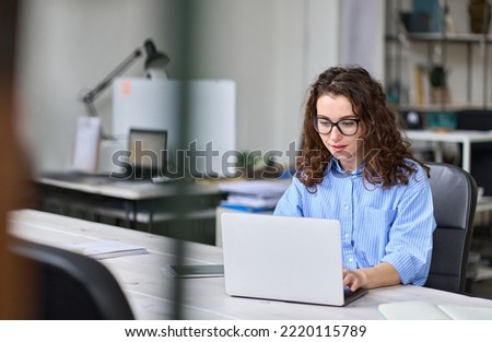 Young business woman company employee worker sitting at desk working online on laptop. Female professional worker manager using computer technology in corporate modern office interior at workplace.