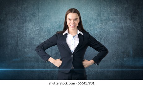 Young Business Woman Dress In Black Suit And White Shirt Is Standing, Holding Her Hands On Hips With Copyspace.