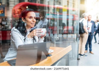 Young Business Woman Drinking Coffee In A Cafe In The City - Woman At The Table With Computer And Coffee, Working From Remote During A Break - Authentic People Lifestyle In London