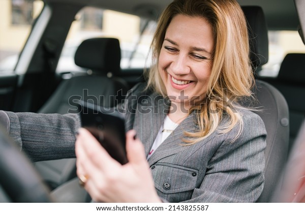 A young business woman drives a company car,\
checks her phone and\
smiling..