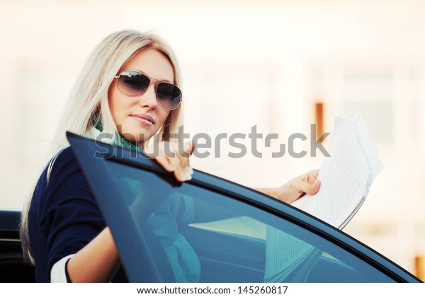 Young\
business woman with financial papers at the\
car