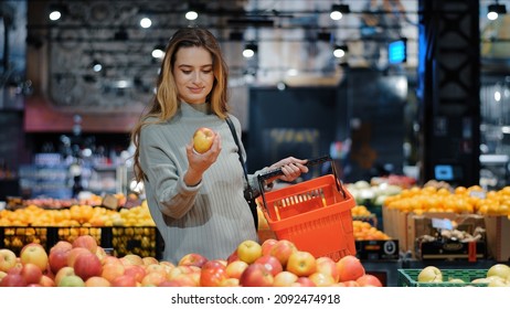 Young business woman girl buyer client blonde lady consumer stands in shop near counter with fruits in grocery store supermarket choosing juicy ripe apples for juice diet food buying puts in basket