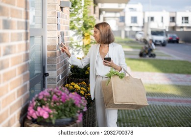 Young business woman going home with groceries, enters a password on the keyboard to access. Concept of modern technologies in everyday life - Powered by Shutterstock