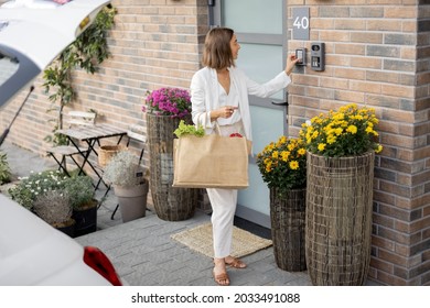 Young business woman going home with groceries, enters a password on the keyboard to access. Concept of modern technologies in everyday life