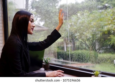 Young Business woman hand touch glass window and looking out of window. working Woman Looking Through Window On Rainy Day and looking for other guy. Young girl looking out the window on a rainy day. - Powered by Shutterstock