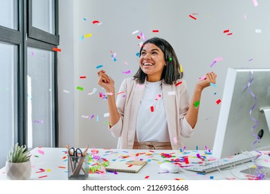 Young business woman having fun time catching confetti sitting at the desk in the office. Party time on the work place. Selective focus. - Shutterstock ID 2126931668