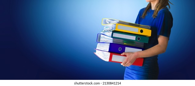 Young business woman holding folder full of paper documents. Office girl assistent with stack of ring binders for archiving documents over blue isolated background.