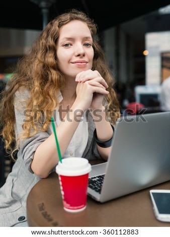 Young business woman with hot beverage and laptop inside coffee store. 
