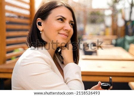 A young business woman inserts an earpiece into her ear to listen to a playlist of music from her smartphone. Wireless mini headphones. Headset and accessories for phones