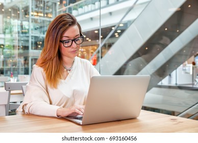 Young business woman with laptop working at open space office in modern interior, freelance concept