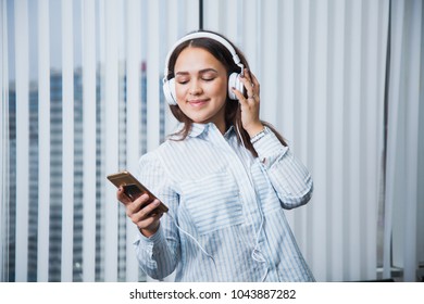 Young Business Woman Listen To Music On Her Leisure Time At Work. Attractive Female Manager At Office With Headphones And Smartphone At Her Workspace