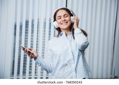 Young Business Woman Listen To Music On Her Leisure Time At Work. Attractive Female Manager At Office With Headphones And Smartphone At Her Workspace