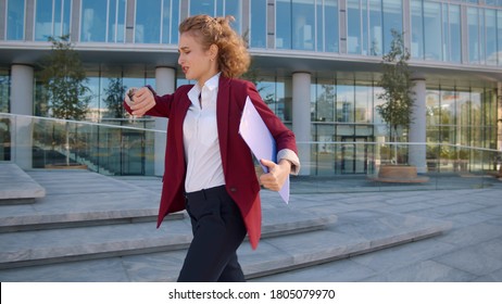 Young Business Woman Looking At Watch And Running Near Office Building Hurry To Meeting. Pretty Lady In Office Wear Late For Work Run Near Business Center