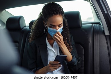 Young business woman in a mask checking her mobile cell phone on a backseat of a taxi during covid-19 quarantine. Business trips during pandemic, new normal and coronavirus travel safety concept. - Powered by Shutterstock