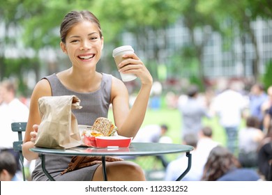 Young business woman on lunch break in City Park drinking coffee and eating sandwich. Happy smiling multiracial young businesswoman in Bryant Park, New York City, USA. - Powered by Shutterstock